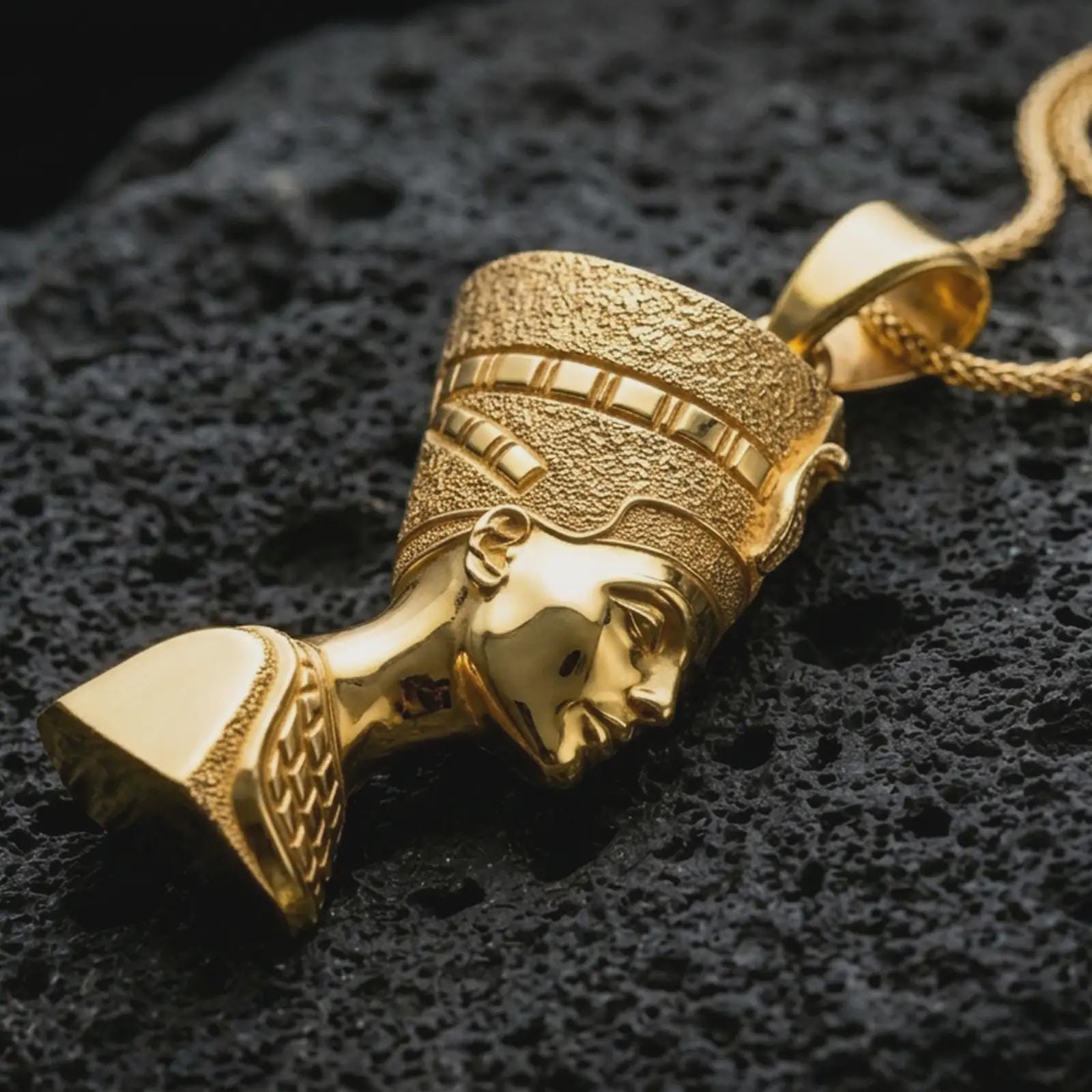 Gold plated Nefertiti pendant necklace presented on porous volcanic rock, highlighting the iconic ancient Egyptian feminine silhouette in a luxurious close-up jewelry image.