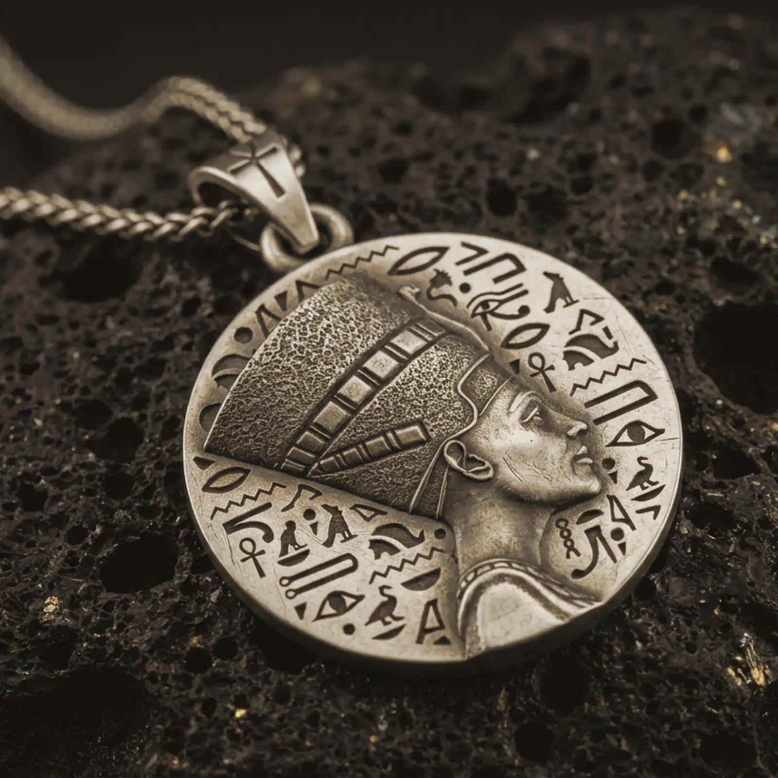 Bronze Nefertiti medallion pendant necklace with an oxidized finish resting on textured volcanic rock, captured in a close-up premium studio composition.