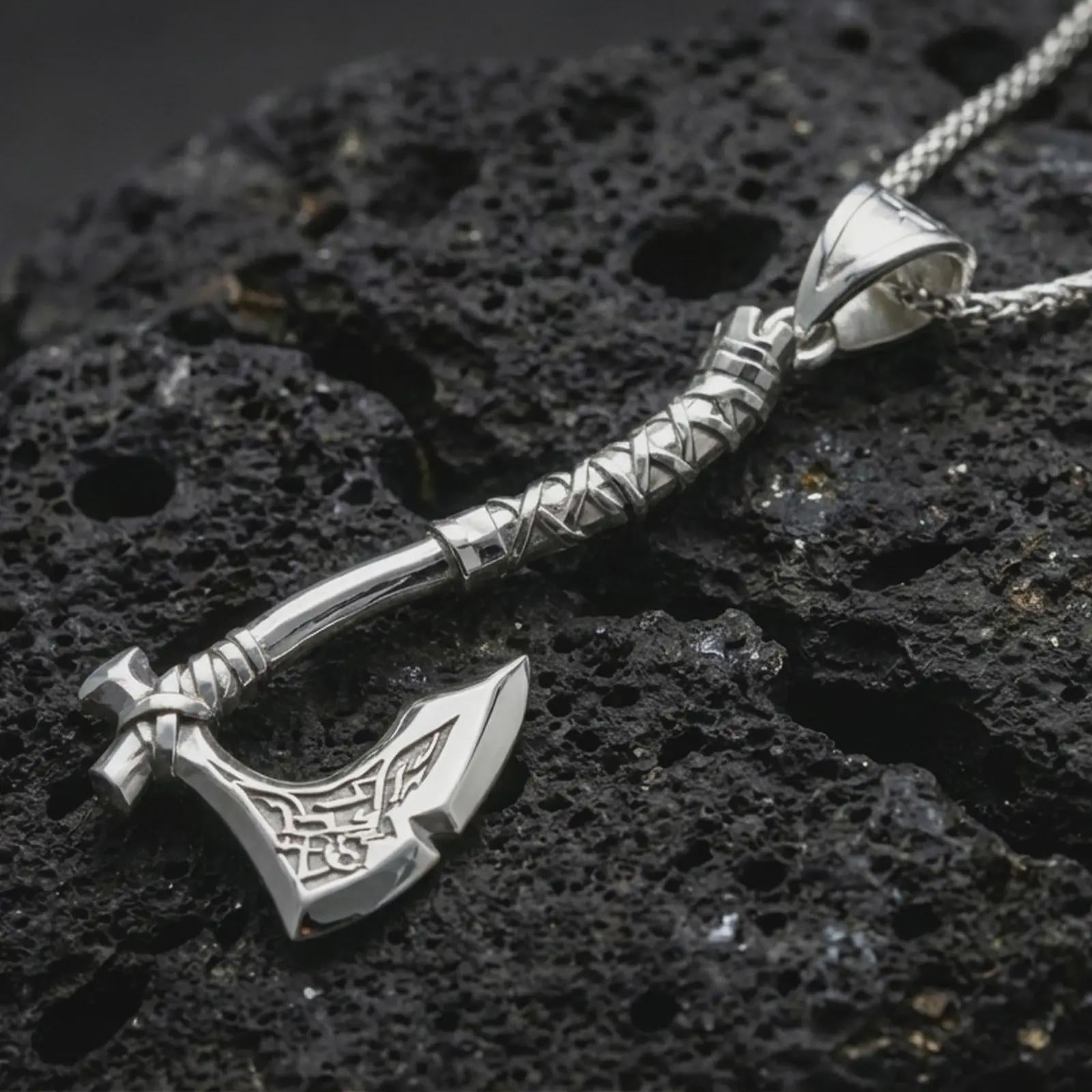 Polished silver battle axe pendant necklace displayed on black volcanic rock, shown in a refined macro product shot with engraved blade details and wrapped handle design.
