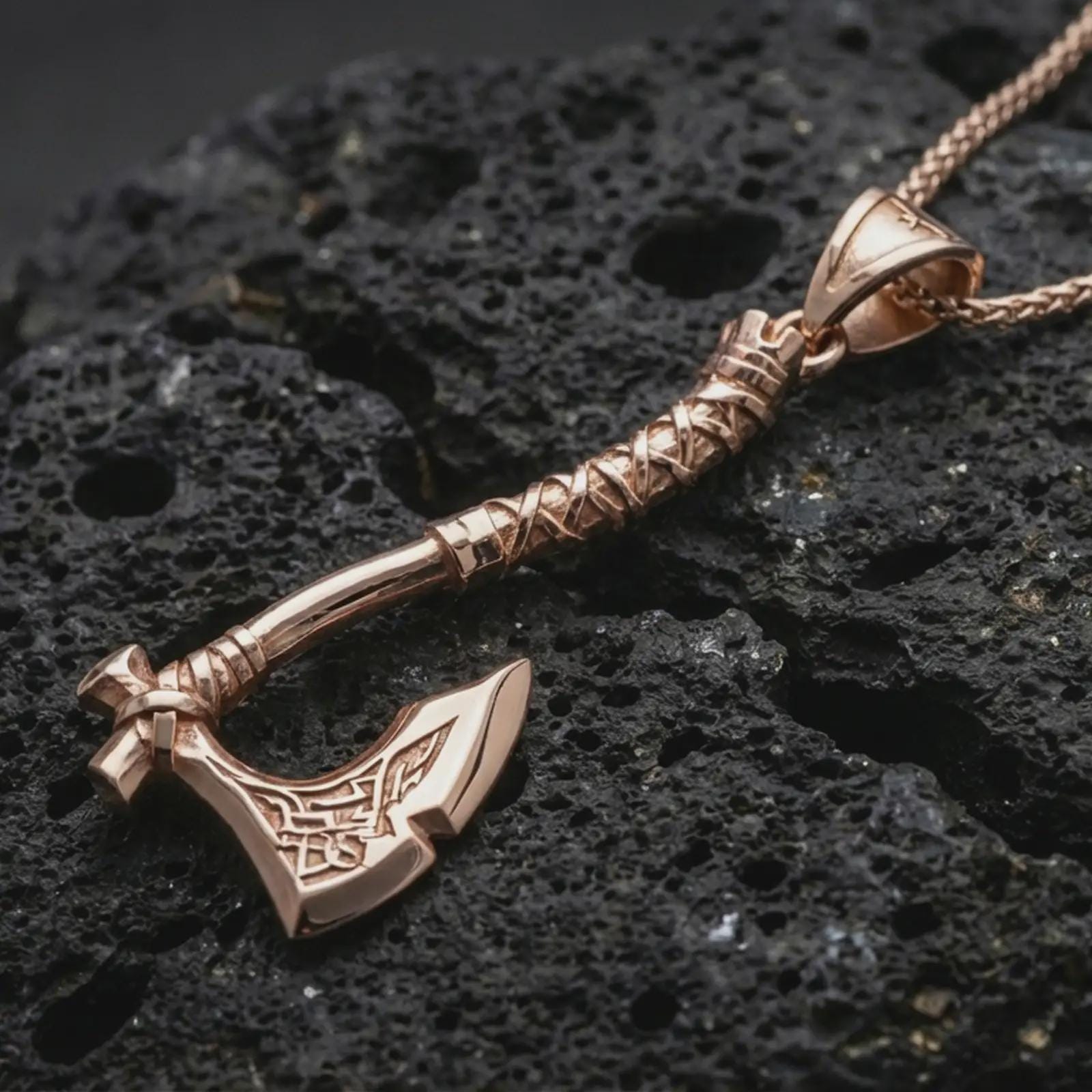 Rose gold plated battle axe pendant necklace on dark volcanic rock, photographed in a detailed premium studio macro view.
