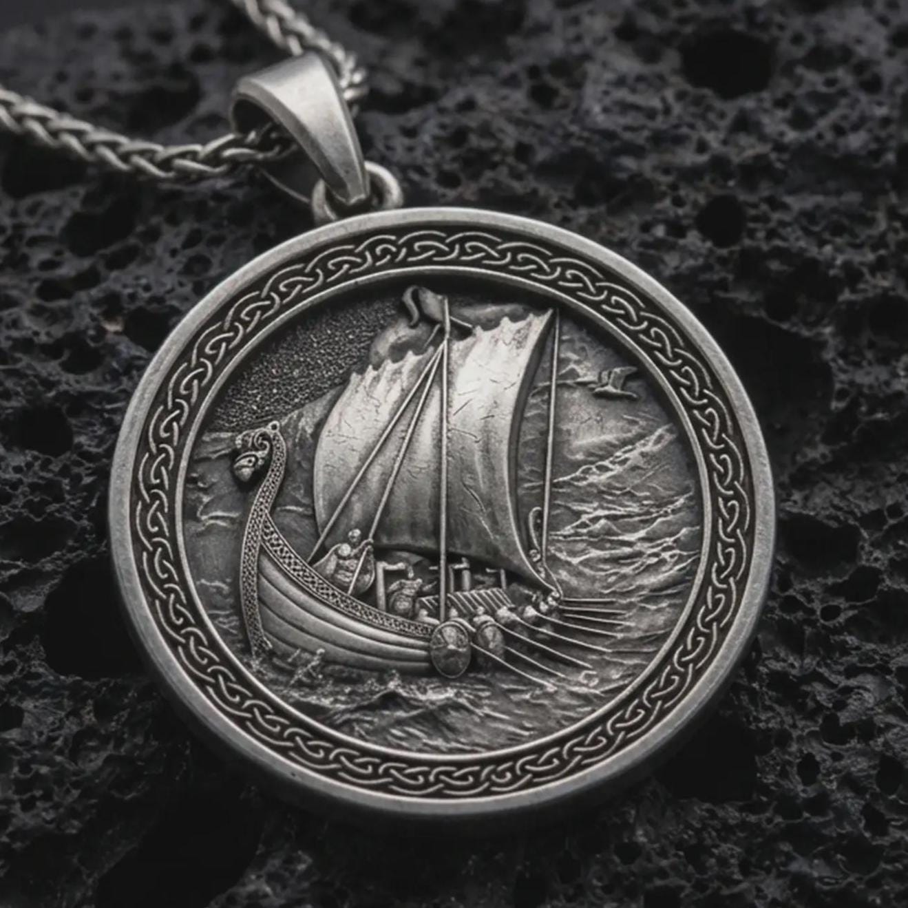 Sterling silver Viking ship pendant necklace with an oxidized finish resting on textured volcanic rock, captured in a close-up premium studio composition.
