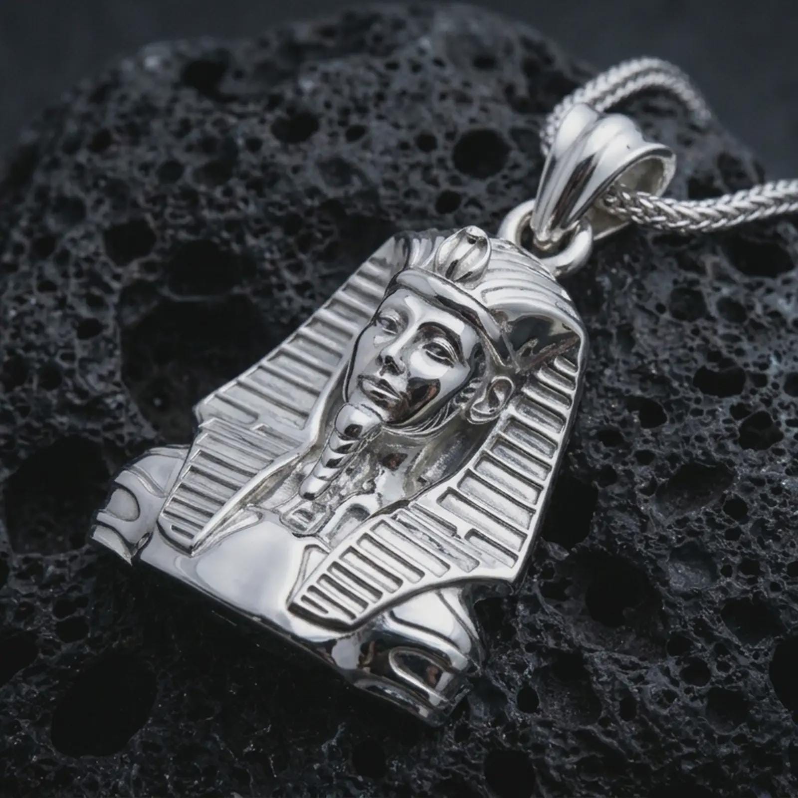 Polished silver Tutankhamun pendant necklace displayed on black volcanic rock, shown in a refined macro product shot with pharaoh headdress, sculptural facial detail, and ancient Egyptian royal styling.