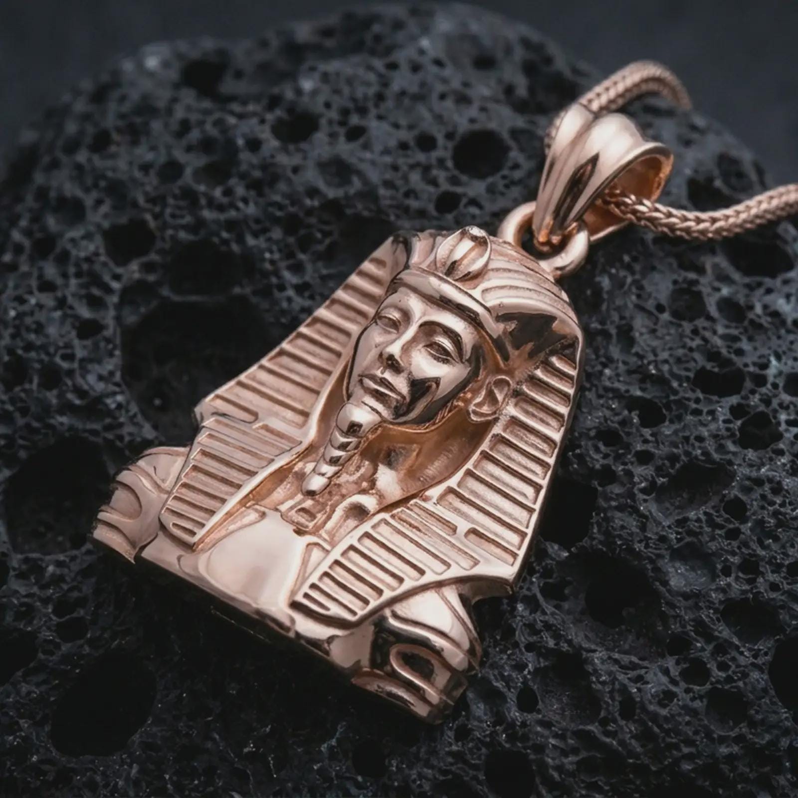 Rose gold plated Tutankhamun pendant necklace on dark volcanic rock, photographed in a detailed premium studio macro view.