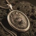 Load image into Gallery viewer, Bronze snarling wolf pendant necklace with an oxidized finish resting on textured volcanic rock, captured in a close-up premium studio composition.
