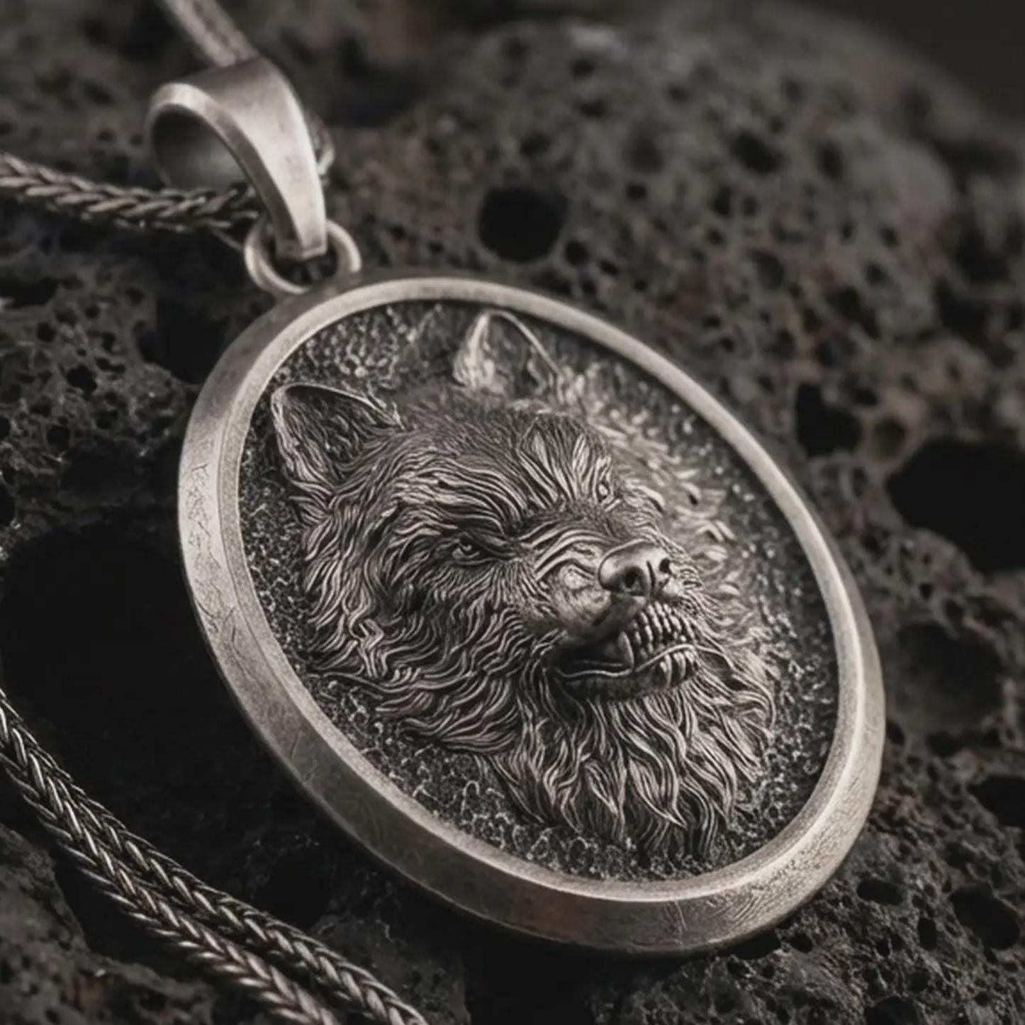 Sterling silver snarling wolf pendant necklace with an oxidized finish resting on textured volcanic rock, captured in a close-up premium studio composition.