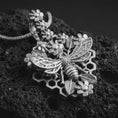 Load image into Gallery viewer, Polished silver floral bee pendant necklace displayed on black volcanic rock, shown in a refined macro product shot with layered flowers, honeycomb design, and realistic bee centerpiece.
