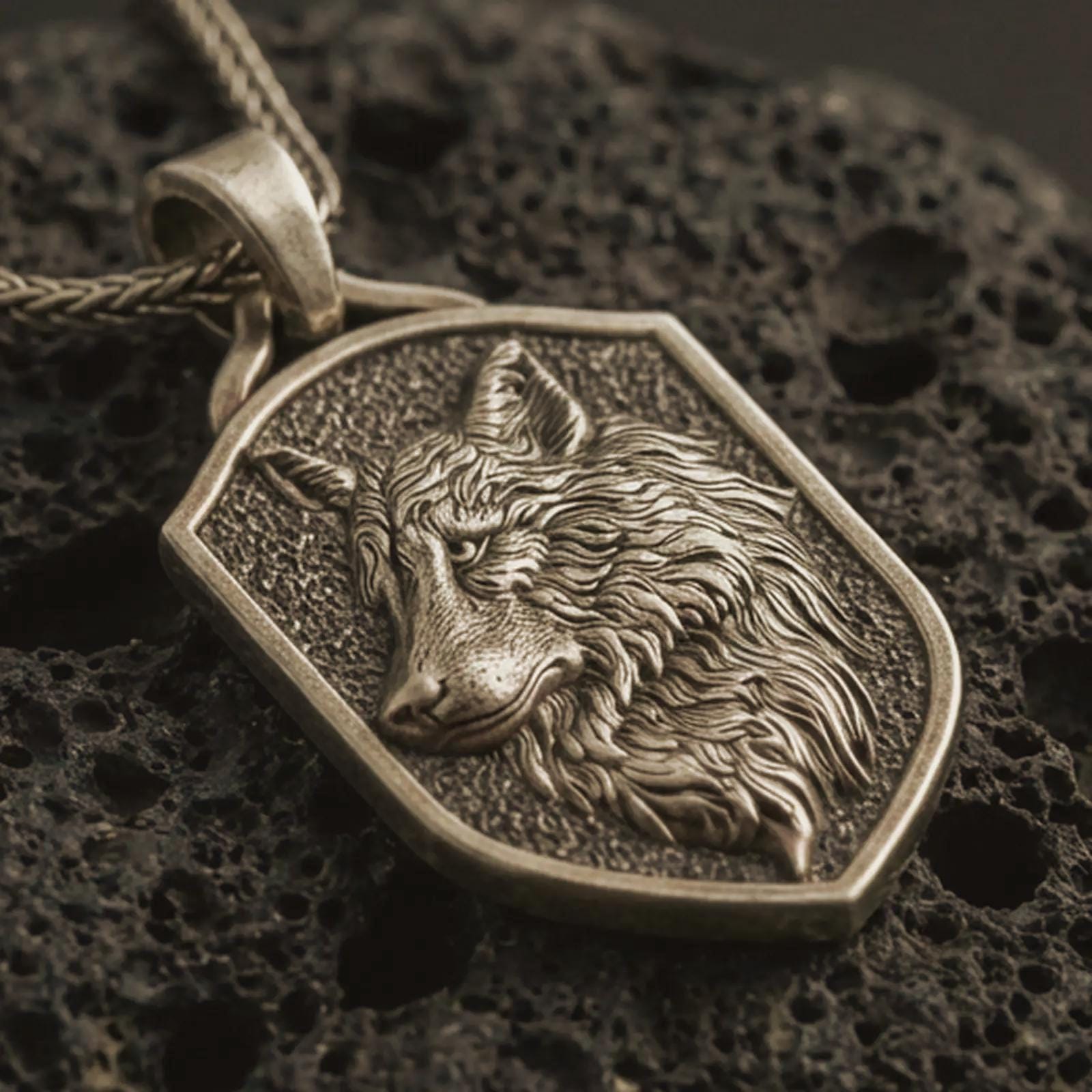 Bronze wolf shield pendant necklace with an oxidized finish resting on textured volcanic rock, captured in a close-up premium studio composition.