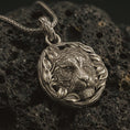 Load image into Gallery viewer, A Bronze tiger pendant on black volcanic stone with oxidized contrast highlighting the leaf wreath frame and engraved stripes.
