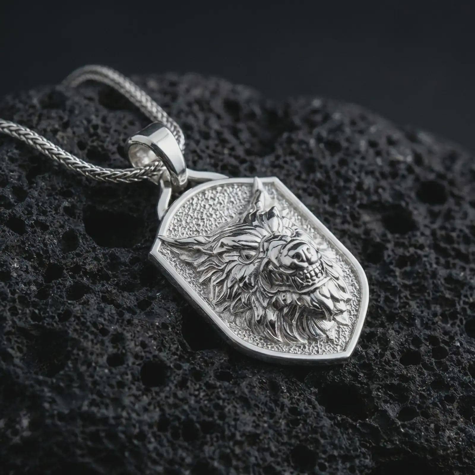 Polished silver ferocious wolf shield pendant necklace displayed on black volcanic rock, shown in a refined macro product shot with aggressive wolf head relief, layered fur detail, and angular shield frame.