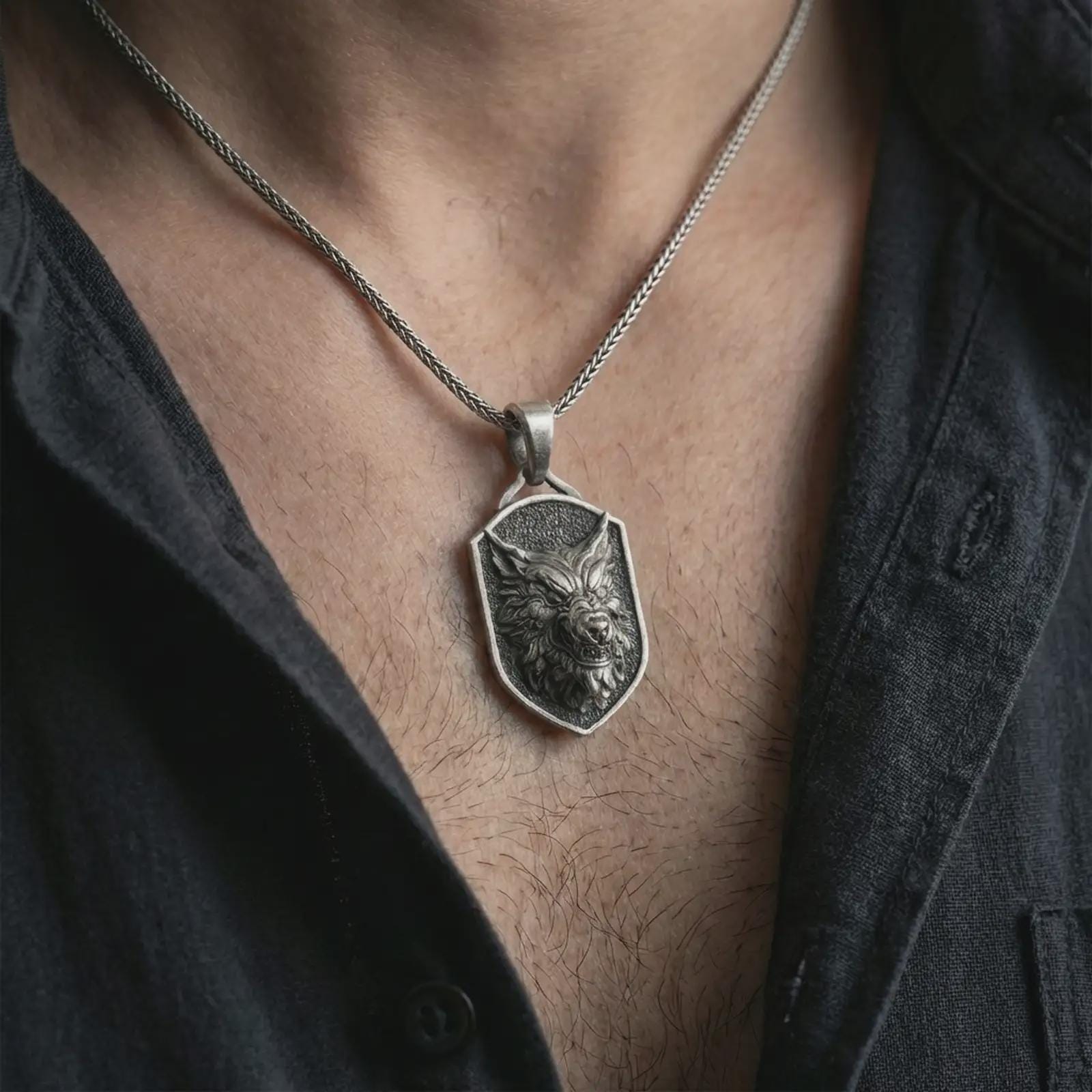 Oxidized ferocious wolf shield pendant necklace worn on the neck, styled in a dark lifestyle portrait with an open shirt and bold masculine presentation.