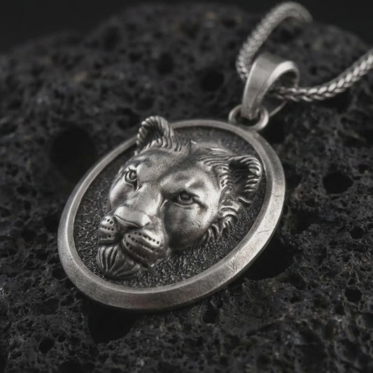 Sterling silver lioness pendant necklace with an oxidized finish resting on textured volcanic rock, captured in a close-up premium studio composition.
