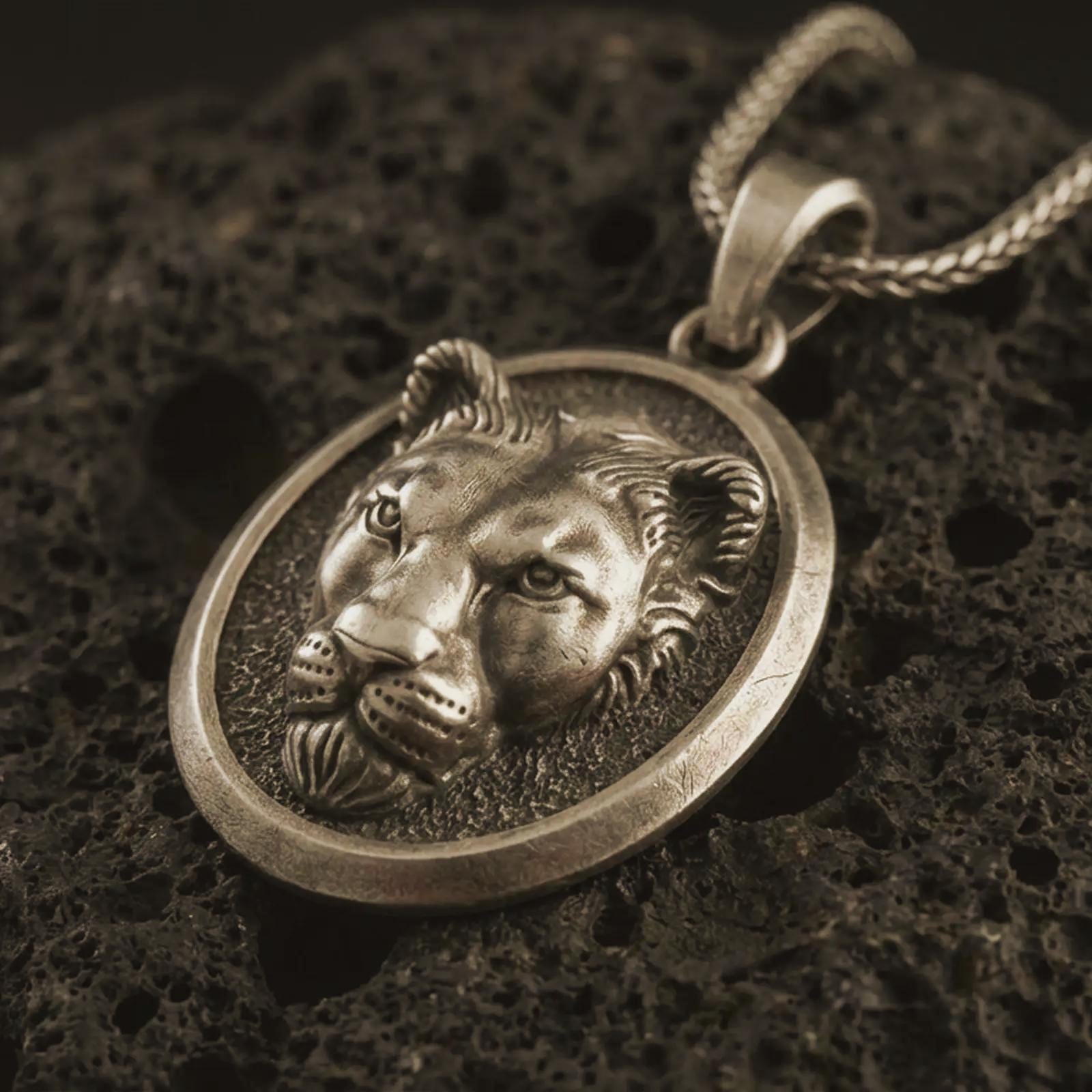 Bronze lioness pendant necklace with an oxidized finish resting on textured volcanic rock, captured in a close-up premium studio composition.