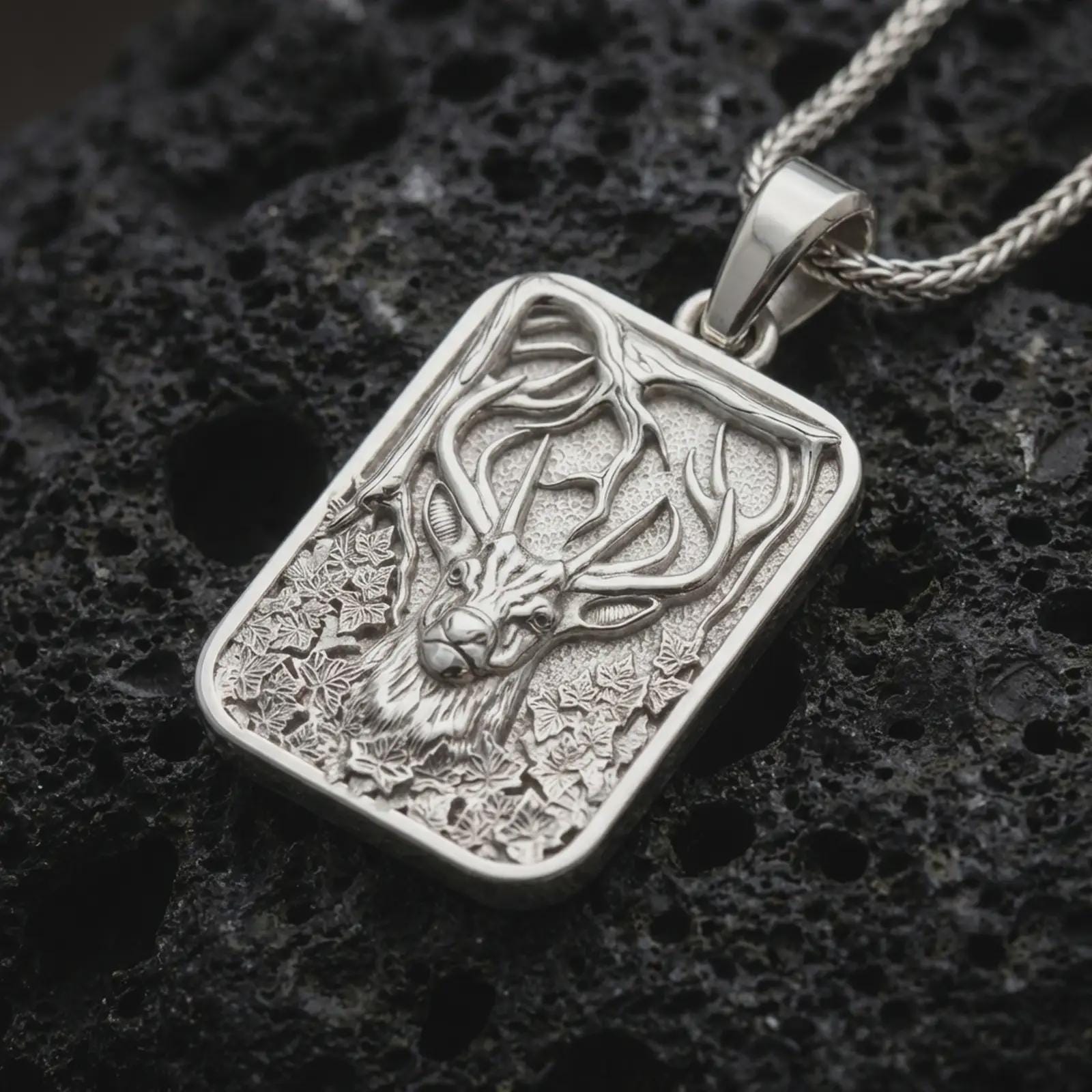 Polished silver stag forest pendant necklace displayed on black volcanic rock, shown in a refined macro product shot with majestic antlers, woodland branches, ivy leaves, and framed nature relief.