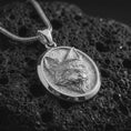 Load image into Gallery viewer, Polished silver fox medallion pendant necklace displayed on black volcanic rock, shown in a refined macro product shot with detailed fur texture, alert ears, and oval frame design.
