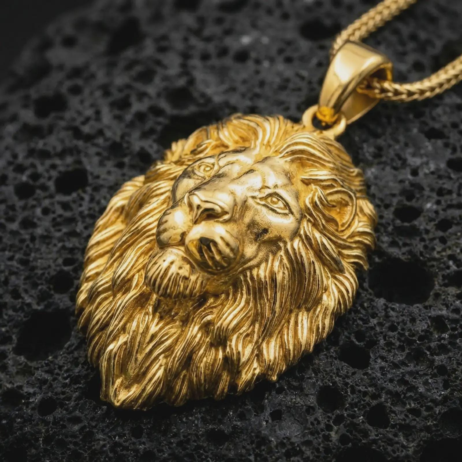 Gold plated lion head pendant necklace presented on porous volcanic rock, highlighting the majestic predator motif in a luxurious close-up jewelry image.