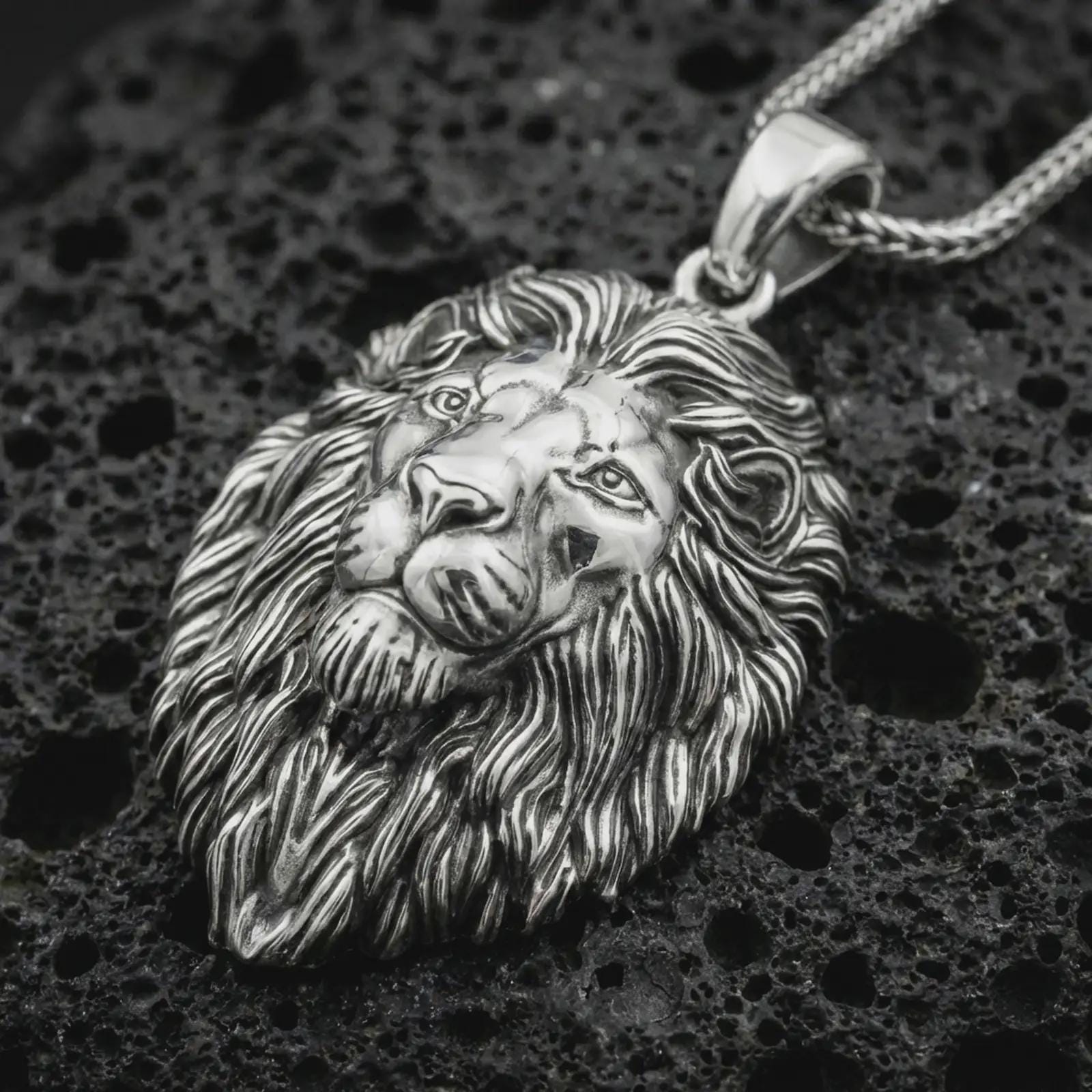 Polished silver lion head pendant necklace displayed on black volcanic rock, shown in a refined macro product shot with realistic facial sculpting, flowing mane detail, and bold wildlife character.