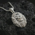 Load image into Gallery viewer, Polished silver roaring lion head pendant necklace displayed on black volcanic rock, shown in a refined macro product shot with open mouth, sharp fang detail, and flowing mane texture.
