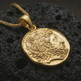 Load image into Gallery viewer, Gold plated ancient Greek coin pendant necklace photographed on porous black volcanic stone, emphasizing the sculpted Hellenic face and irregular coin silhouette in a luxury jewelry composition.
