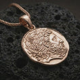 Load image into Gallery viewer, Rose gold plated ancient Greek coin pendant necklace presented on textured volcanic stone, showcasing the artistic Greek profile relief and weathered historical medallion form in a macro studio shot.
