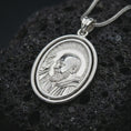 Load image into Gallery viewer, Polished silver Saint Padre Pio spinning pendant necklace displayed on dark volcanic rock, shown in a premium close-up image that highlights the saint portrait, halo, and layered oval frame.
