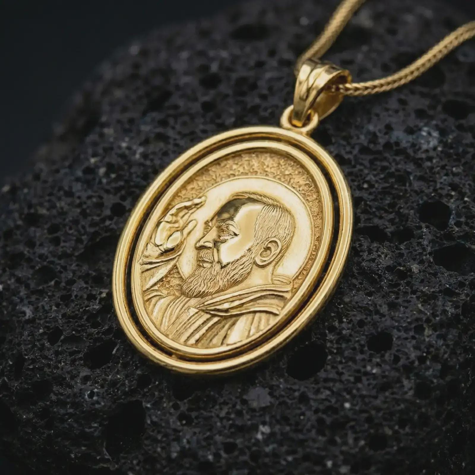 Gold plated Saint Padre Pio spinning pendant necklace photographed on porous black volcanic stone, emphasizing the Catholic saint relief and elegant rotating medallion design in a luxury jewelry composition.