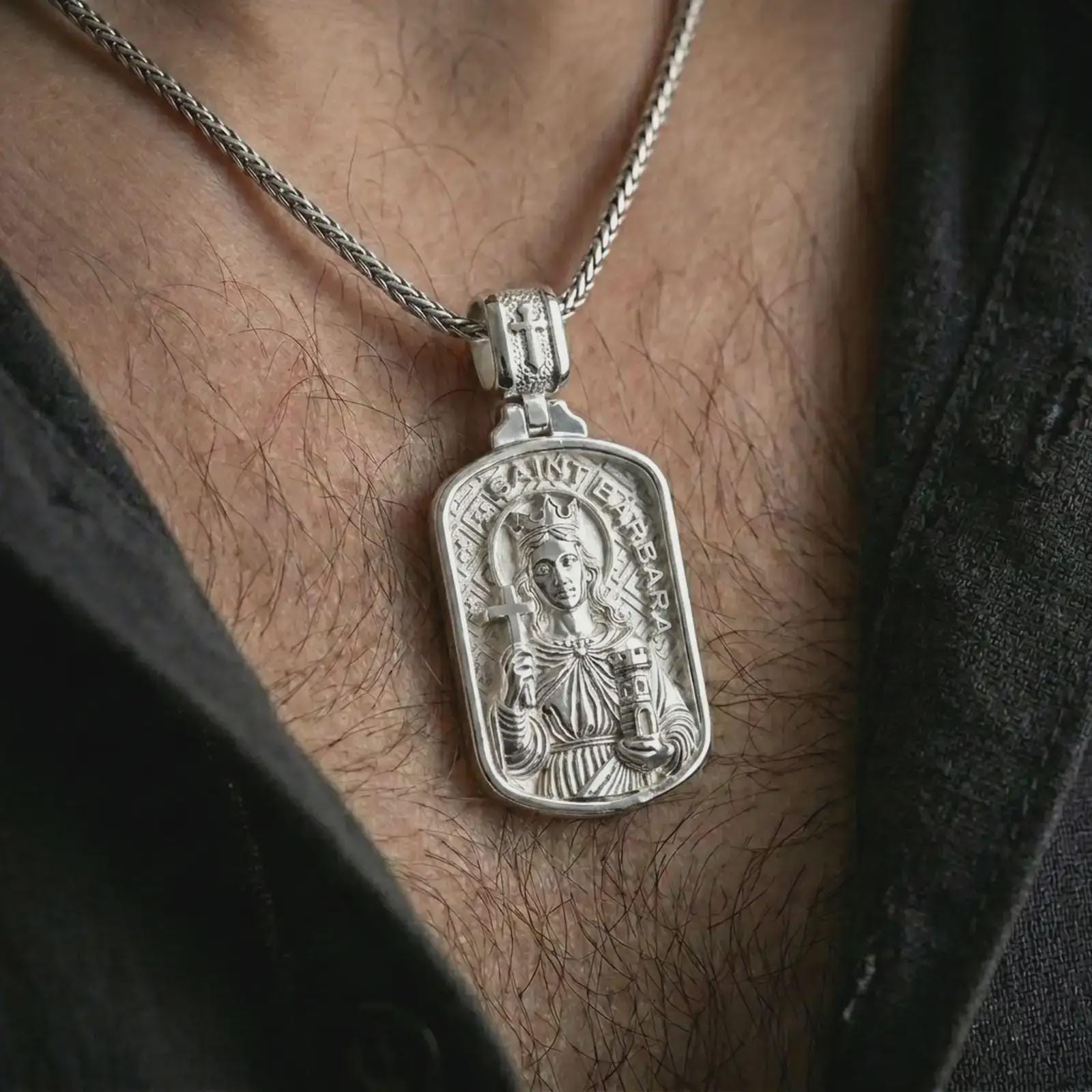 Polished silver Saint Barbara pendant necklace worn on the chest, masculine lifestyle shot highlighting the saint relief, cross, tower detail, and bright silver finish.