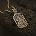 Load image into Gallery viewer, Bronze Saint Barbara pendant necklace on textured volcanic rock, close-up studio shot highlighting the saint relief, cross, tower detail, and dark antique silver contrast.
