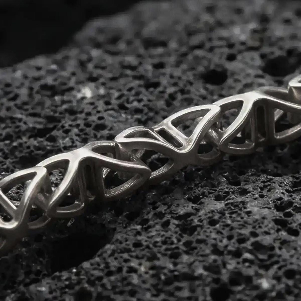 Sterling silver DNA helix chain necklace with an oxidized finish resting on textured volcanic rock, captured in a close-up premium studio composition.