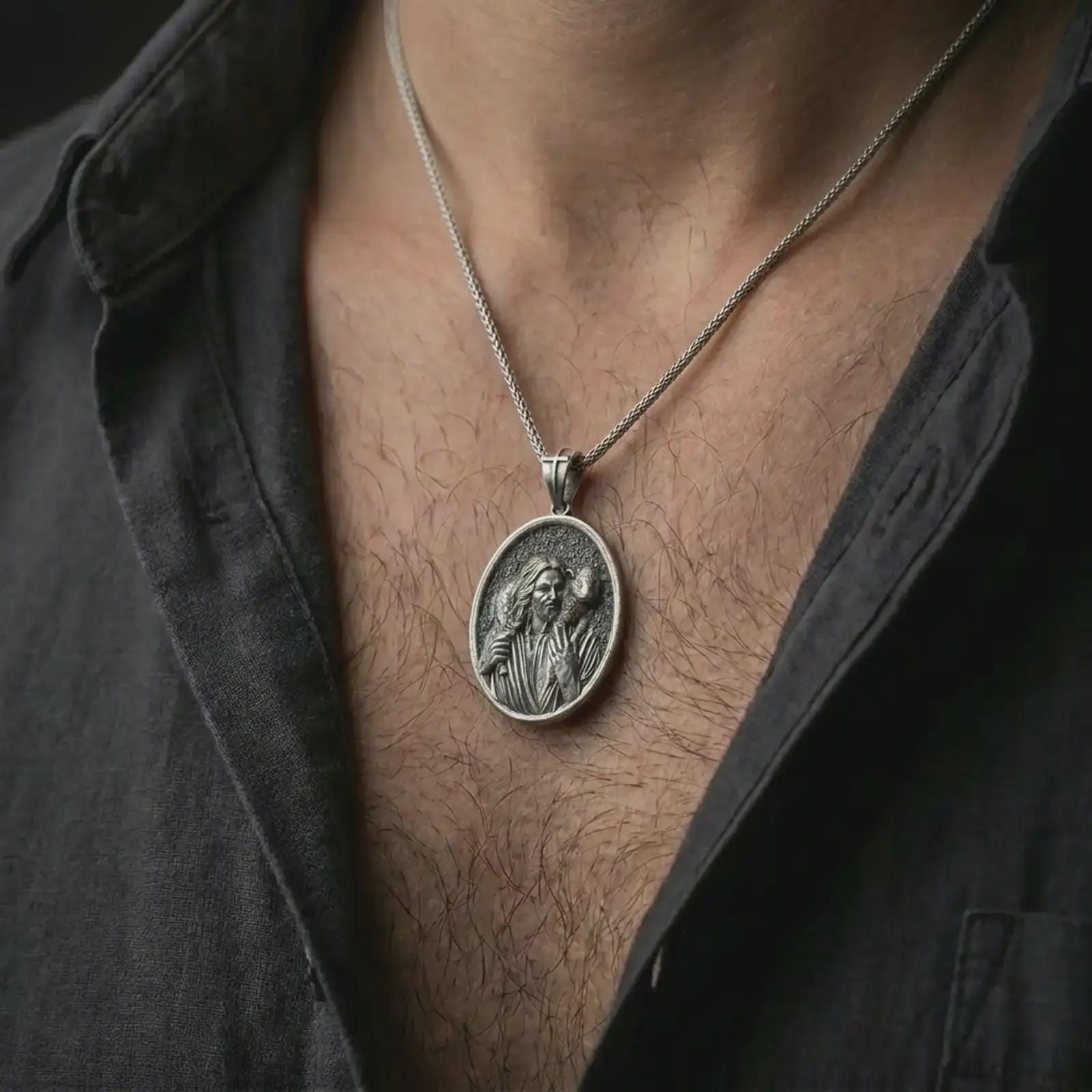 Oxidized Good Shepherd Jesus pendant necklace worn on the chest, close-up lifestyle jewelry photo showing the religious medallion on a spiga chain with dark clothing.
