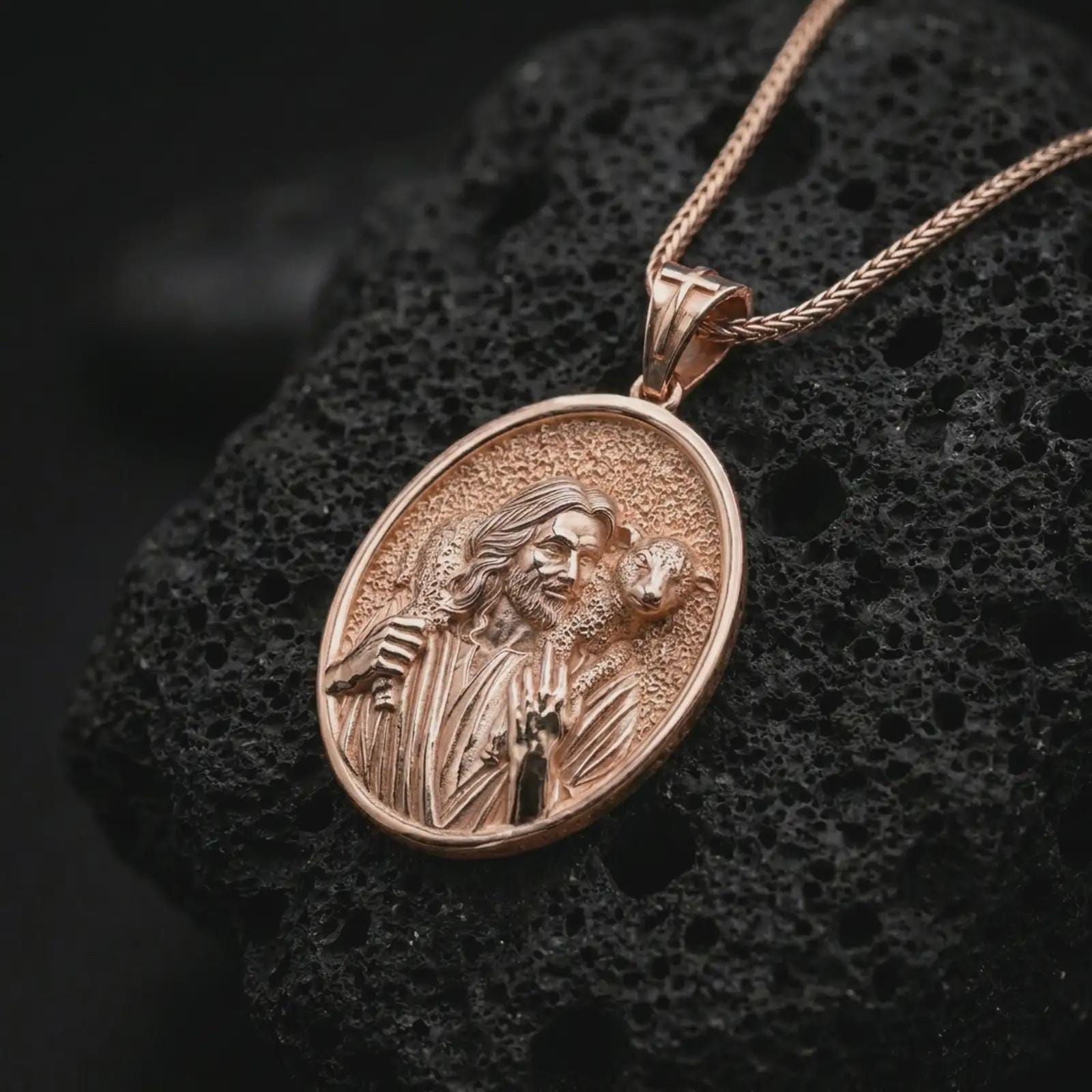 Rose gold plated Good Shepherd Jesus pendant necklace on textured volcanic rock, detailed macro product shot with soft warm reflections and sacred shepherd symbolism.