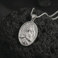 Load image into Gallery viewer, Polished silver Saint Joan of Arc pendant necklace on textured volcanic rock, centered macro jewelry photo with detailed Catholic medal engraving and bright silver highlights.
