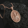 Load image into Gallery viewer, Rose gold plated Saint Patrick pendant necklace on textured volcanic rock, detailed macro product shot with soft warm reflections and devotional Irish saint symbolism.

