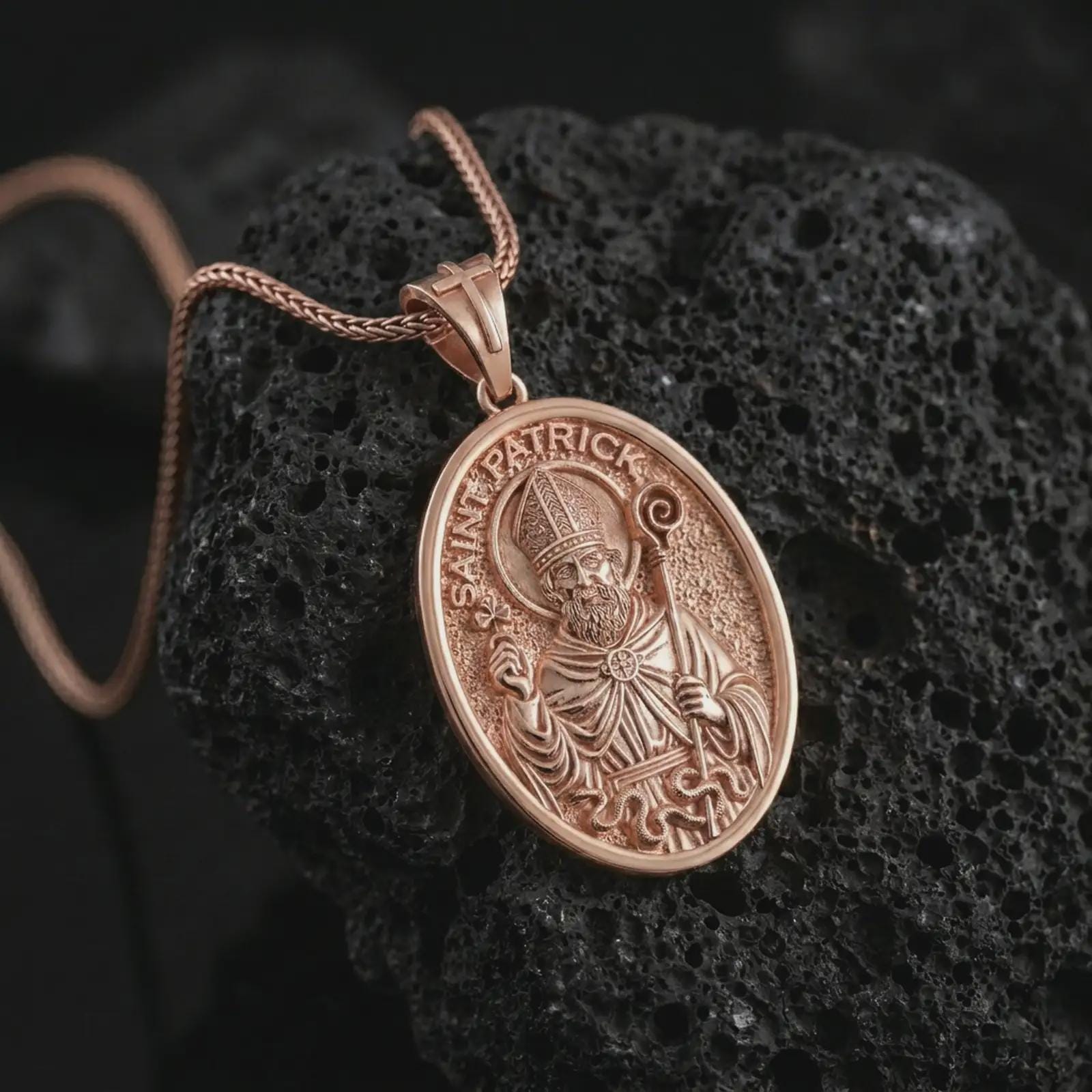 Rose gold plated Saint Patrick pendant necklace on textured volcanic rock, detailed macro product shot with soft warm reflections and devotional Irish saint symbolism.