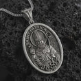 Load image into Gallery viewer, Oxidized Saint Patrick pendant necklace on textured volcanic rock, close-up studio shot highlighting the bishop relief, shamrock, staff, and antique silver contrast.
