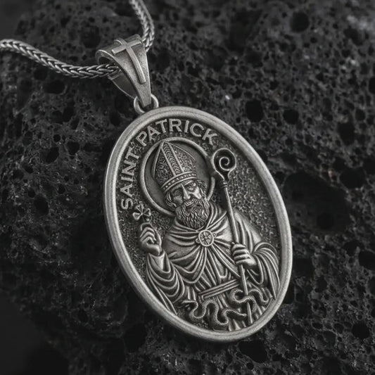 Oxidized Saint Patrick pendant necklace on textured volcanic rock, close-up studio shot highlighting the bishop relief, shamrock, staff, and antique silver contrast.