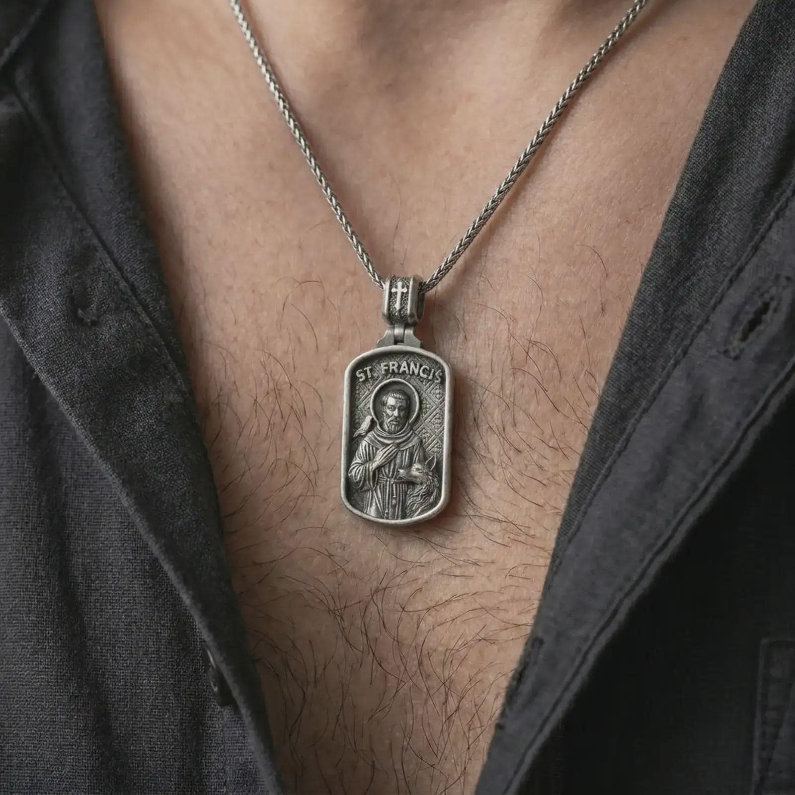 Oxidized Saint Francis pendant necklace worn on the chest, close-up lifestyle jewelry photo showing the religious medallion on a spiga chain with dark clothing.