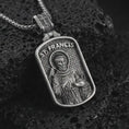 Load image into Gallery viewer, Oxidized Saint Francis pendant necklace on textured volcanic rock, close-up studio shot highlighting the saint relief, bird, wolf detail, and antique silver contrast.
