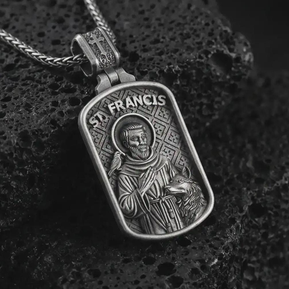 Oxidized Saint Francis pendant necklace on textured volcanic rock, close-up studio shot highlighting the saint relief, bird, wolf detail, and antique silver contrast.