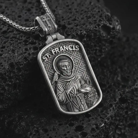 Oxidized Saint Francis pendant necklace on textured volcanic rock, close-up studio shot highlighting the saint relief, bird, wolf detail, and antique silver contrast.