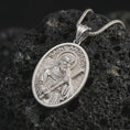 Load image into Gallery viewer, Polished silver Saint Andrew pendant necklace on textured volcanic rock, centered macro jewelry photo with detailed religious medal engraving and bright silver highlights.
