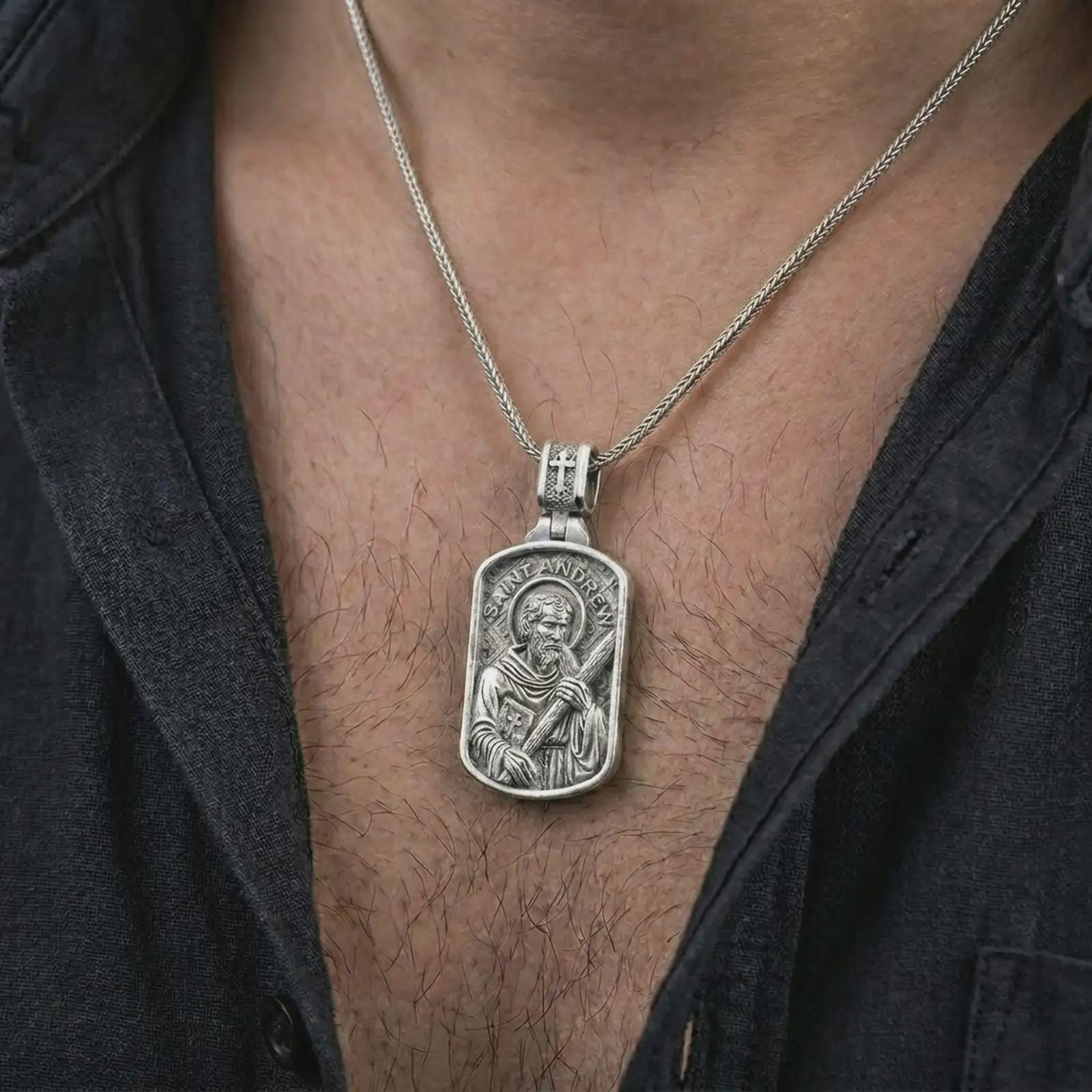 Polished silver Saint Andrew dog tag pendant necklace worn on the chest, masculine lifestyle shot highlighting the apostle relief, cross, book detail, and bright silver finish.