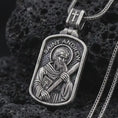 Load image into Gallery viewer, Oxidized Saint Andrew dog tag pendant necklace on textured volcanic rock, close-up studio shot highlighting the apostle relief, cross, book detail, and antique silver contrast.
