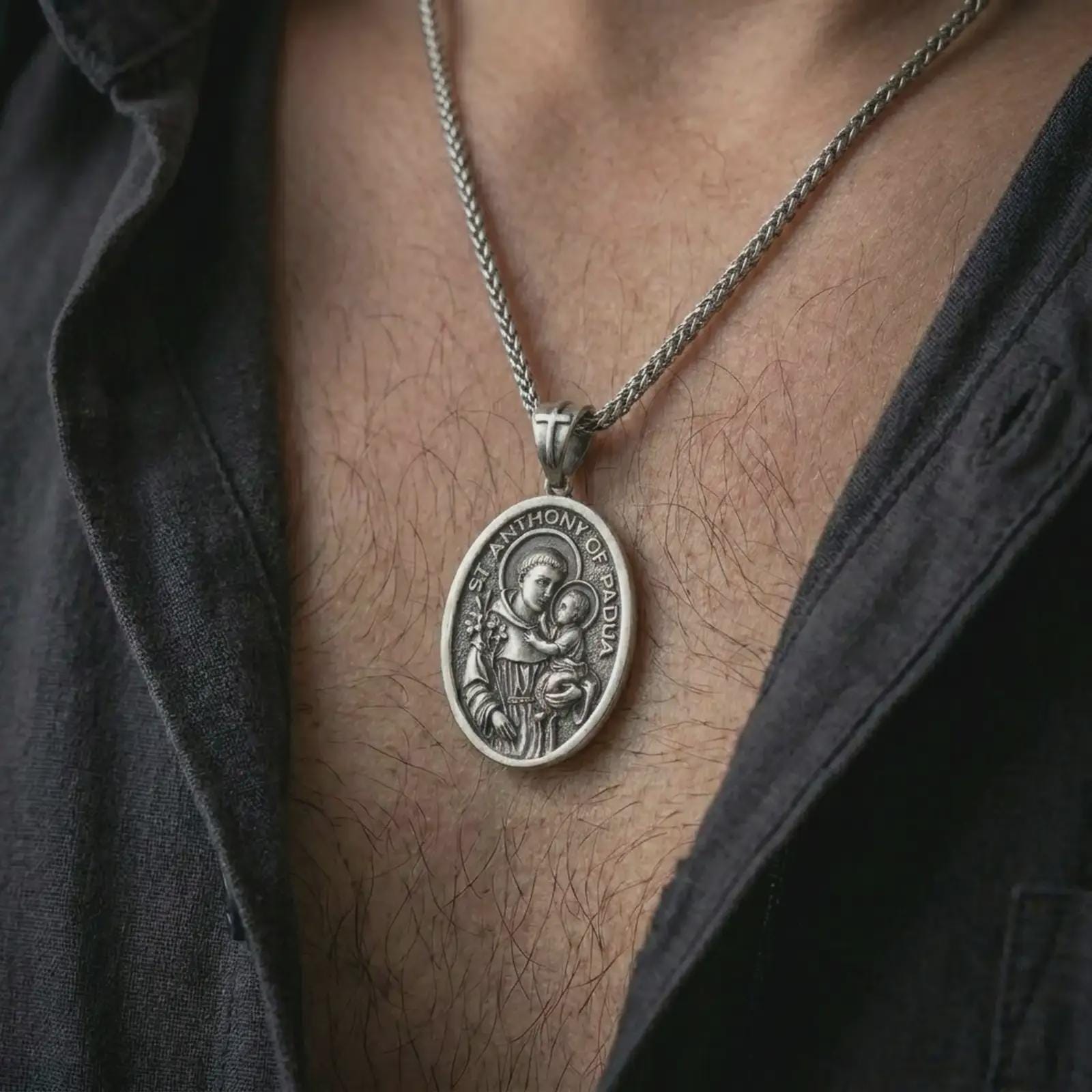 Oxidized Saint Anthony of Padua pendant necklace worn on the chest, close-up lifestyle jewelry photo showing the Catholic medallion on a spiga chain with dark clothing.