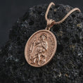 Load image into Gallery viewer, Rose gold plated Saint Roch pendant necklace on textured volcanic rock, detailed macro product shot with soft warm reflections and devotional healing saint design.
