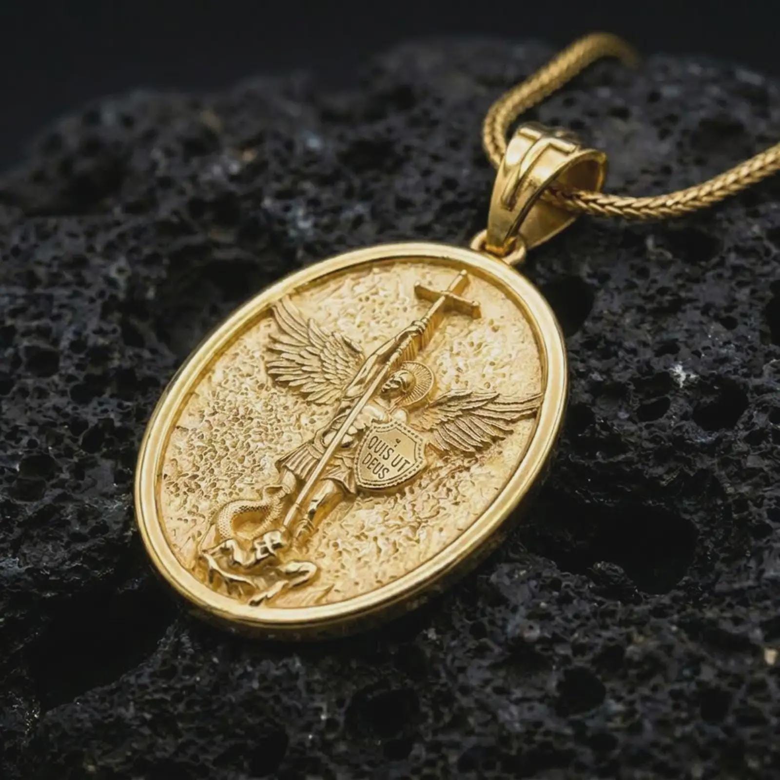 Gold plated Saint Michael pendant necklace on textured volcanic rock, premium close-up studio composition emphasizing the winged archangel, sword, and shield symbolism.