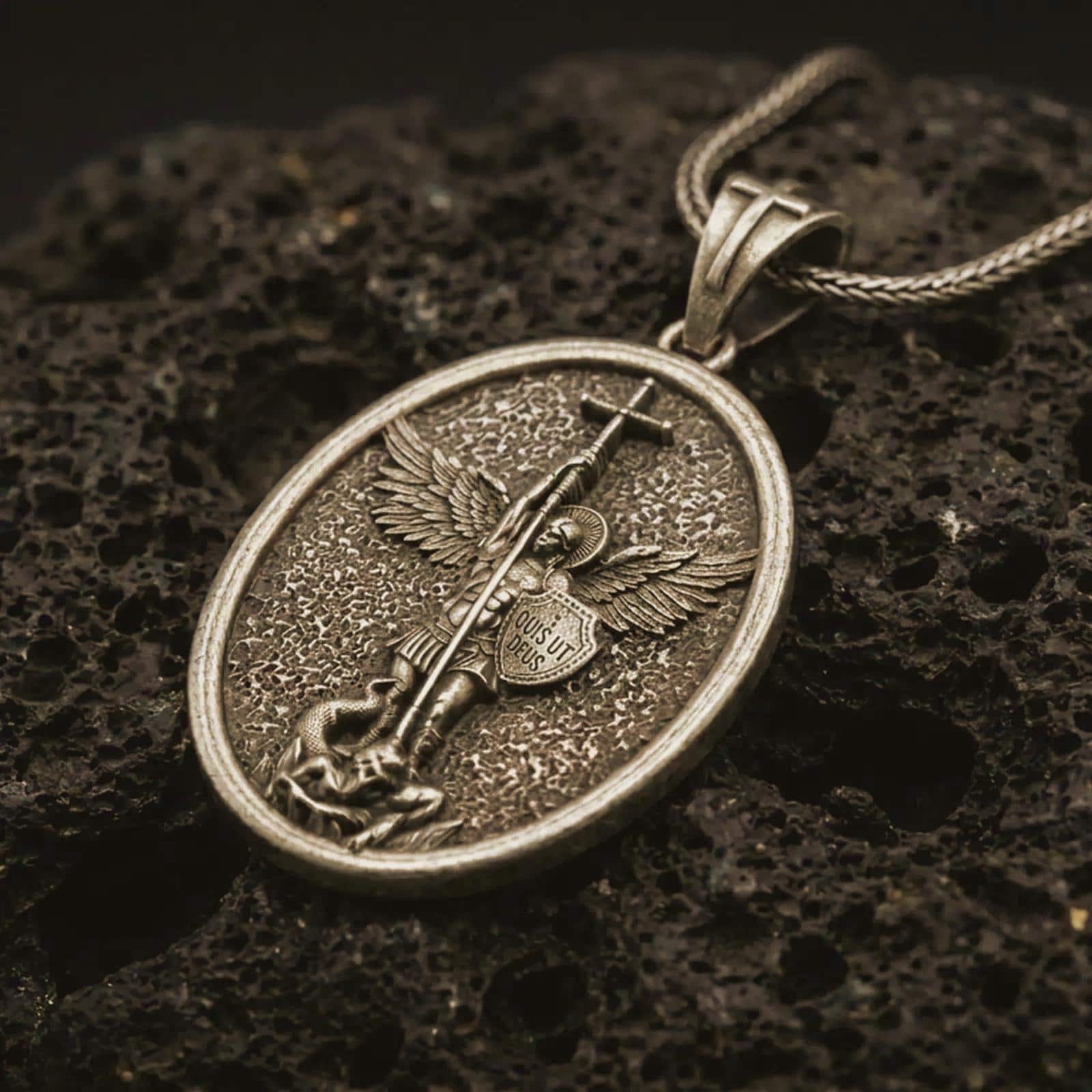 Bronze Saint Michael pendant necklace on textured volcanic rock, close-up studio shot highlighting the sword, wings, shield, fallen demon detail, and antique silver contrast.