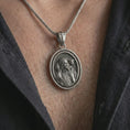 Load image into Gallery viewer, Oxidized spinning Good Shepherd pendant necklace worn on the chest, close-up lifestyle jewelry photo showing the religious medallion on a spiga chain with dark clothing.
