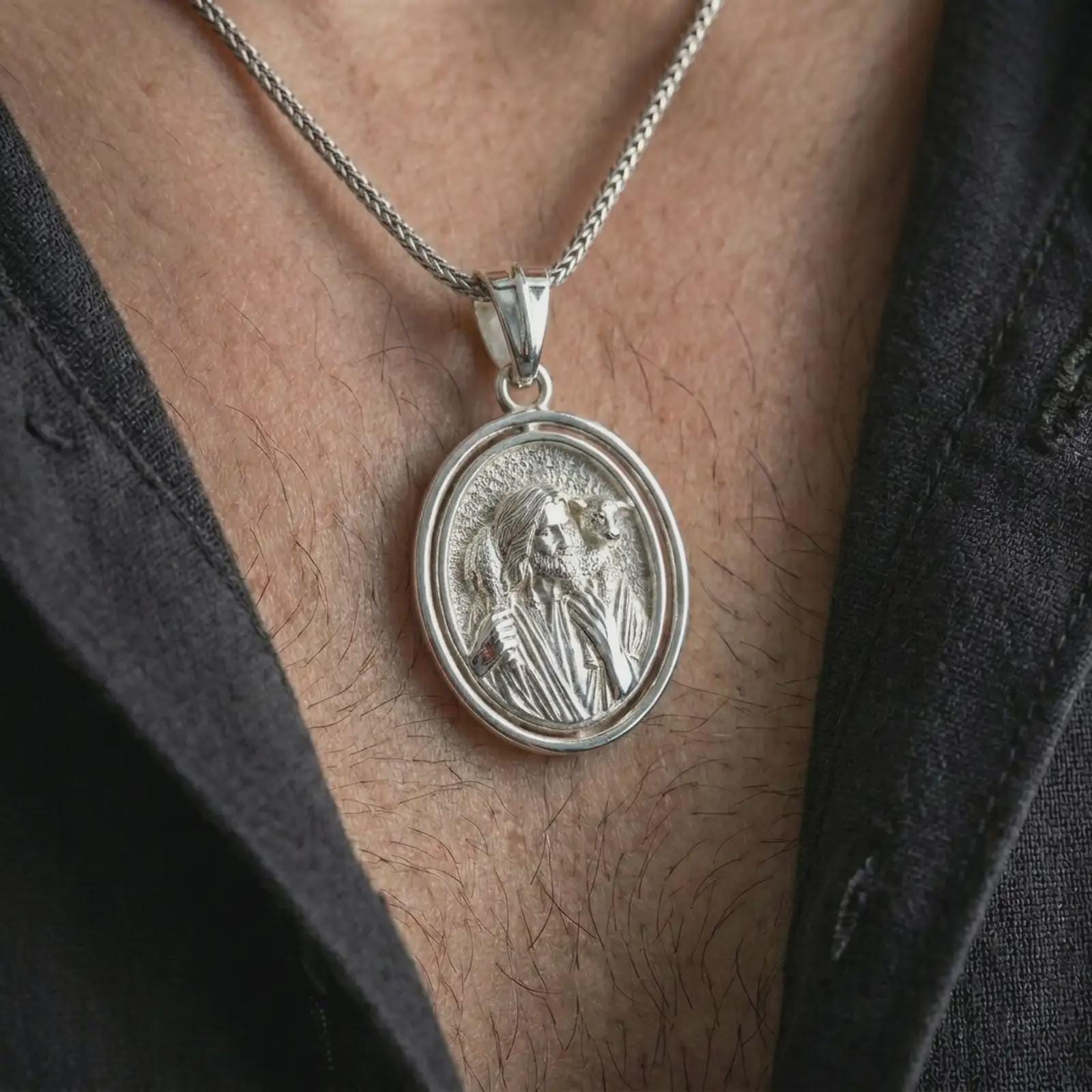 Polished silver spinning Good Shepherd pendant necklace worn on the chest, masculine lifestyle shot highlighting the Jesus and lamb relief with bright silver finish.