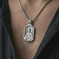 Load image into Gallery viewer, Polished silver Saint James the Apostle pendant necklace worn on the chest, masculine lifestyle shot highlighting the apostle relief, halo, book detail, and bright silver finish.
