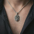 Load image into Gallery viewer, Oxidized cobra shield pendant necklace worn on the neck, styled in a dark lifestyle portrait with an open shirt and bold symbolic presentation.
